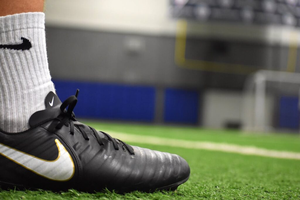 A detailed shot of a soccer cleat on an indoor turf field, emphasizing footwear and athletic activity.